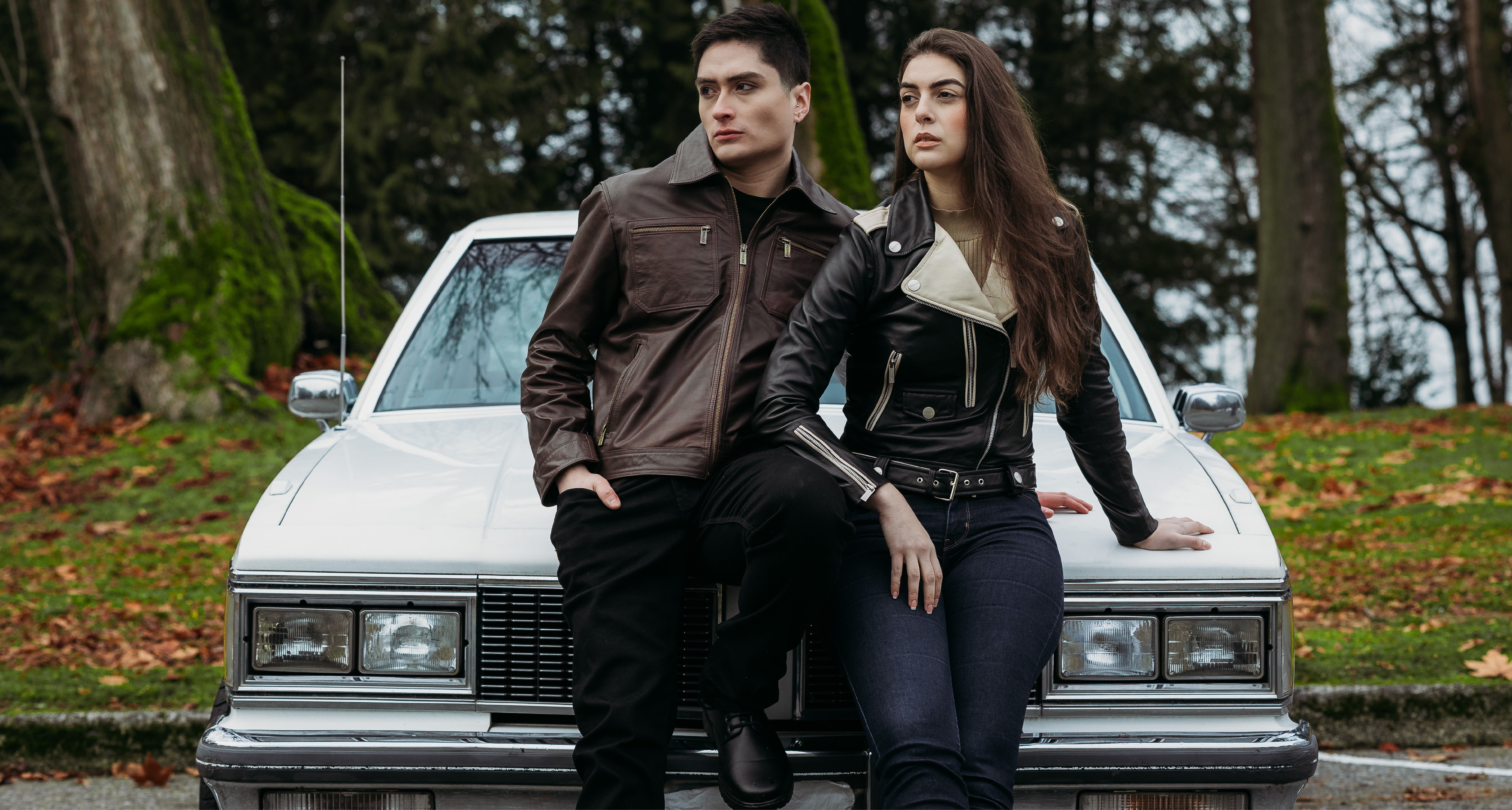 Peroye male and female models sitting by a car in the background wearing brown and black + off white leather jackets respectively.