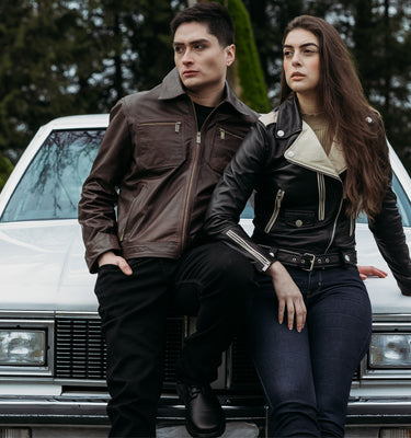 Peroye male and female models sitting by a car in the background wearing brown and black + off white leather jackets respectively.